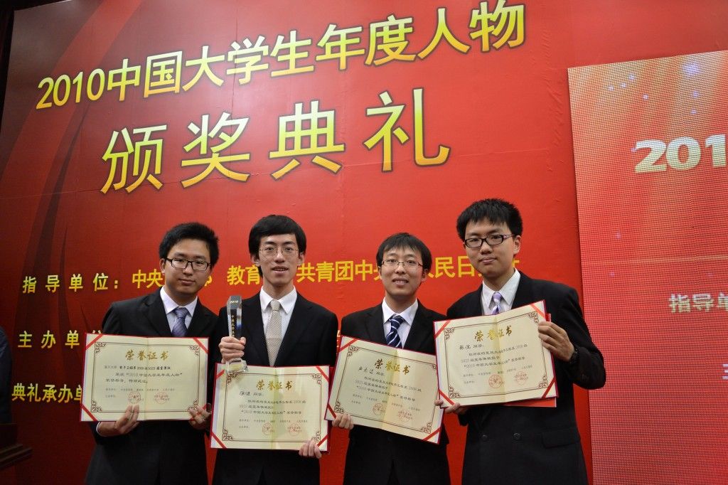 Four students in suits holding award certificates on stage.